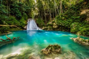 Cascading waterfalls surrounded by lush green vegetation with people climbing the tiers of the falls in Dunn's River Falls, Jamaica.