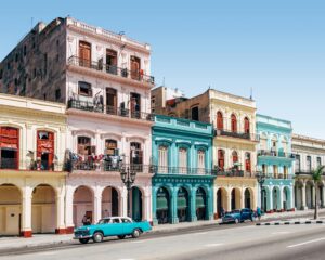 A vibrant street scene in Havana, Cuba, showcasing colorful colonial buildings in shades of turquoise, yellow, and pink.